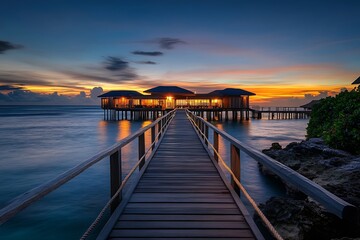 Wooden pier leading to illuminated overwater bungalow at dusk, golden hour sky