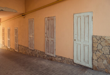Passage with six old wooden doors. Long corridor under a building with peach color walls and row of...