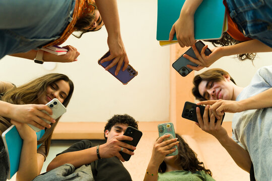 Low angle view of a group of high school students using smartphones and holding notebooks