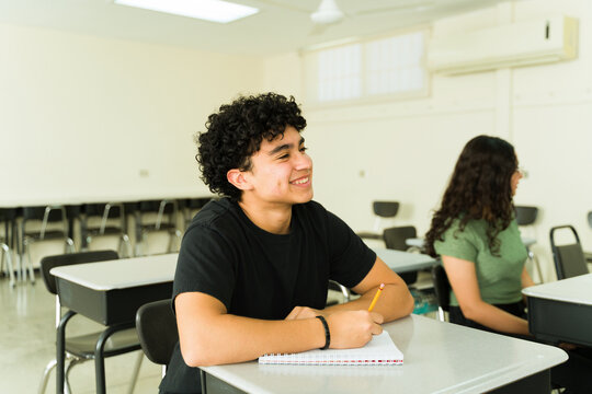 Happy high school student taking notes in classroom