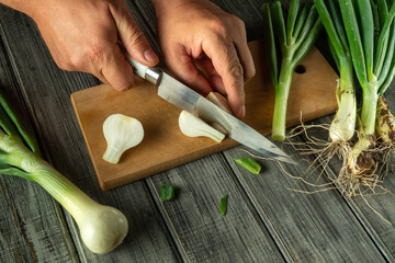Hands skillfully cut fresh green onions on a wooden board. The vibrant colors of the vegetables pop...