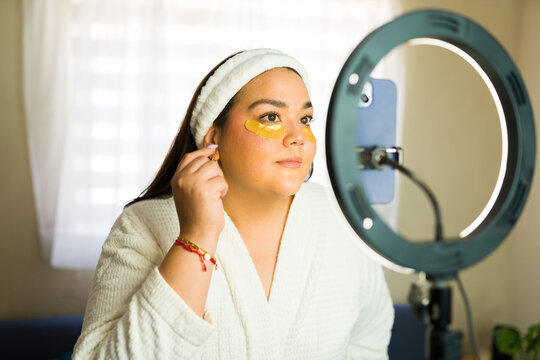 Plus size woman applying golden eye patches and recording a beauty tutorial