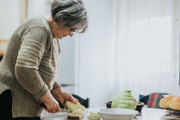 A senior woman is seen chopping fresh cabbage in a kitchen while preparing a meal, emphasizing her activity and independence.