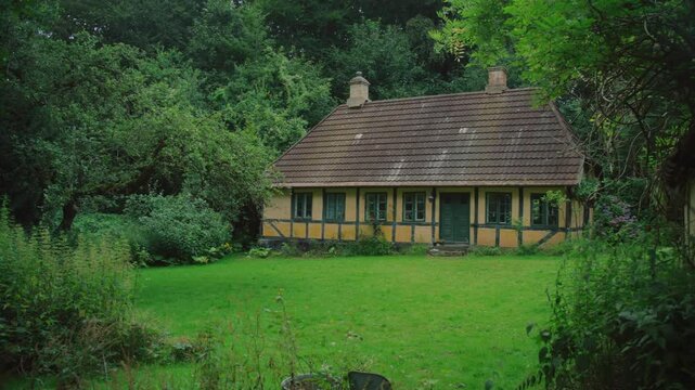 A picturesque yellow cottage surrounded by lush greenery, nestled in Langeland, Denmark