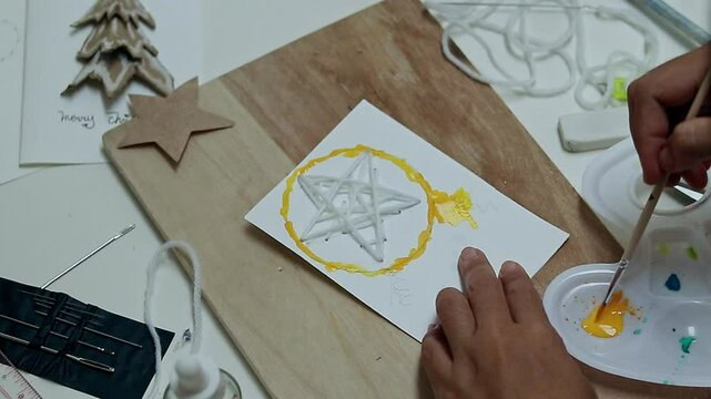 A person paints a parol or traditional Philippine star lantern as a handmade design for a Filipino Christmas greetings card, holiday craft project