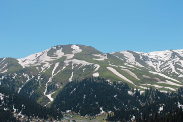 snow covered mountain with forest and little village on the bottom side in Georgia Baxmaro