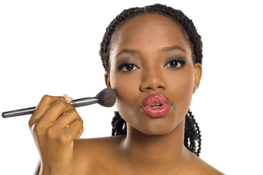 Black woman talking while applying makeup with brush, expressive beauty tutorial concept, studio shot on white background.