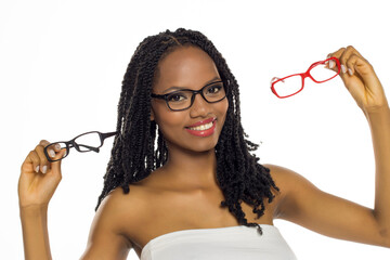 Black woman choosing between different eyeglasses while smiling, studio shot on white background.