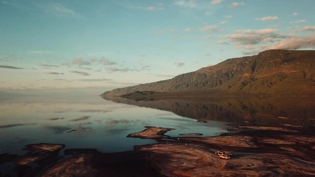 Stunning Golden Light Hitting Mountains surrounding Lake Natron at Sunrise with Mirror Reflection and Flocks of Flamingos