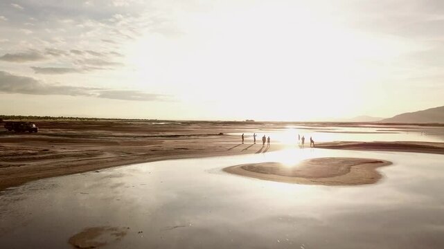 4k drone footage flying over Lake Natron towards the golden sun in the early hours of the morning with silhouettes of cars, people and flamingos
