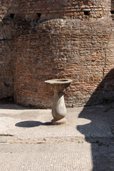 Ancient stone pedestal with a basin in front of a weathered brick wall casting shadows