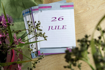 Calendar for July 26: numbers 26, name of the month July in English on a flip calendar among flowers