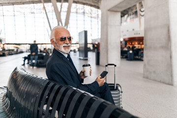 Mature Businessman Relaxing at Airport with Coffee and Smartphone