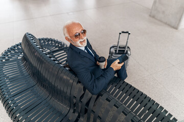 Senior Businessman Relaxing in Airport Lounge with Smartphone and Coffee