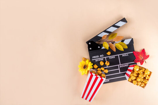 Autumn seasonal movie marathon. Cozy fall season cinema and TV-show Movie Night party. Cinema clapper-board, sweet pumpkin syrup caramel popcorn in paper cups, autumn leaves, pumpkins and decorations - Powered by Adobe