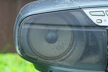 front of old black plastic stereo tape music recorder with buttons and one round  diffuser electric speaker in protective grille during daytime outdoors