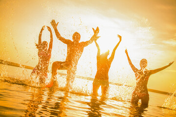 group of young people happily jump and splash in the sea at sunset Silhouettes.