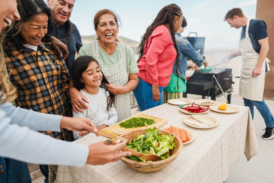 Multi generational people doing barbecue at home's rooftop - Multiracial friends having fun eating and cooking during weekend day - Summer and food concept - Main focus on kid face