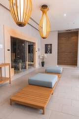 Modern spa area in a boutique hotel featuring wooden loungers with blue cushions, a glass enclosed sauna, pendant lights, and decorative accents.