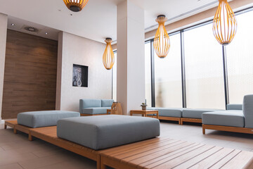 Luxurious hotel lounge featuring light blue cushioned seating, wooden accents, pendant lights, frosted glass windows, and minimalist decor.