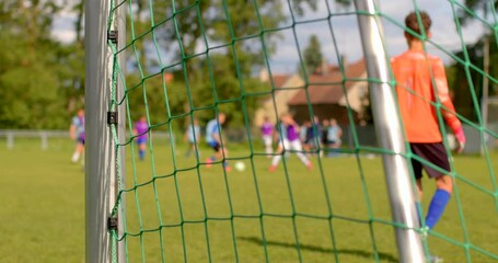 Dynamic frames of a youth soccer match behind the goalpost, capturing thrilling action with players, including the goalkeeper and midfielders, showcasing impressive skills and teamwork - Powered by Adobe