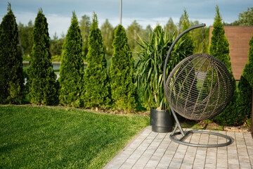 Outdoor patio with hanging wicker chair surrounded by bright green trees and grass