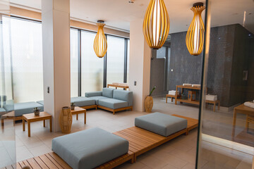 Luxurious spa interior featuring light wooden furniture, blue gray cushions, pendant lights, frosted glass windows, and a visible sauna area.