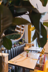 Dining area features marble topped tables, cushioned chairs, yellow curtains, a white brick wall, and a curved shelving unit with plants and decor.
