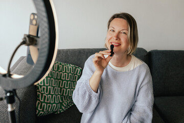 Middle-aged woman beauty blogger filming skincare product unboxing at home with ring light....