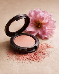 Peach blush compact rests elegantly beside delicate pink flower, with slight dusting of powder scattered around. soft hues evoke sense of beauty and freshness