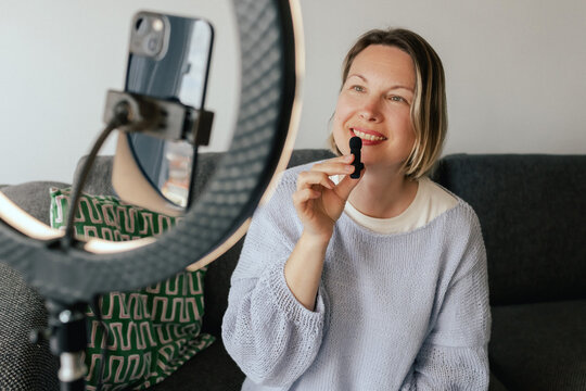 Middle-aged woman beauty blogger filming skincare product unboxing at home with ring light. User-generated content UGC for online store promotion. Vlogger live streaming. Part of a series