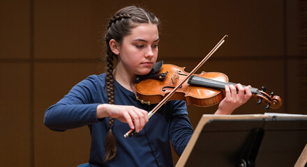 teen girl playing violin solo with focus in concert hall  