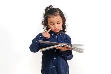 A little Asian girl thinking about something while looking at a book