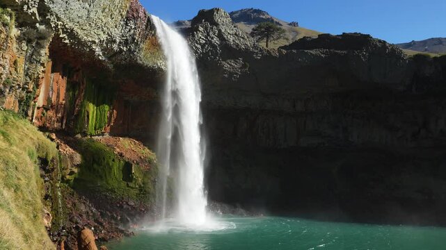 Powerful Salto del Agrio waterfall cascades into a vibrant turquoise pool, framed by rugged. Neuquen, Argentina
