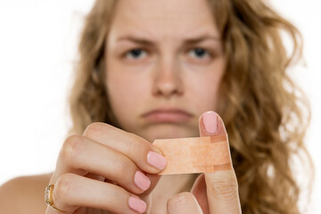 Woman looking frustrated, holding adhesive bandage with a focused expression. Blurred background suggesting minor injury or discomfort