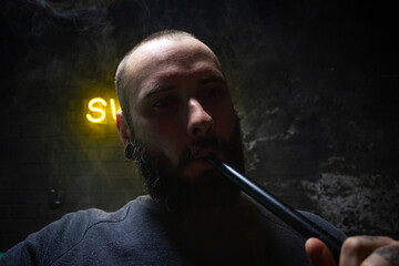 bearded man smoking a hookah in a dark room. hookah lifestyle and smoking concept. portrait of a sailor with a hookah close up view