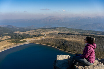 Naklejka premium Woman sitting on rock with scenic view from Batea Mahuida and Alumine Lake. Villa Pehuenia, Neuquen, Argentina