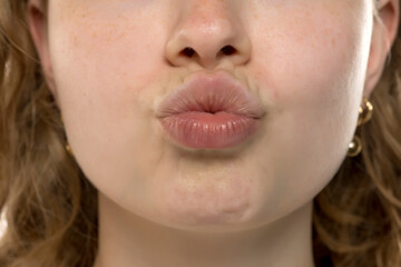 Close-up of young woman making pucker or kissing gesture. Plump lips, natural texture, soft focus....