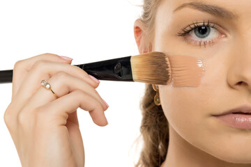 Close-up of woman applying liquid foundation with flat makeup brush on cheek, showing professional...