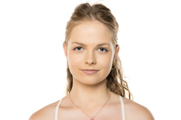 Portrait of young woman with blue eyes and wavy hair in ponytail, wearing white top and delicate...