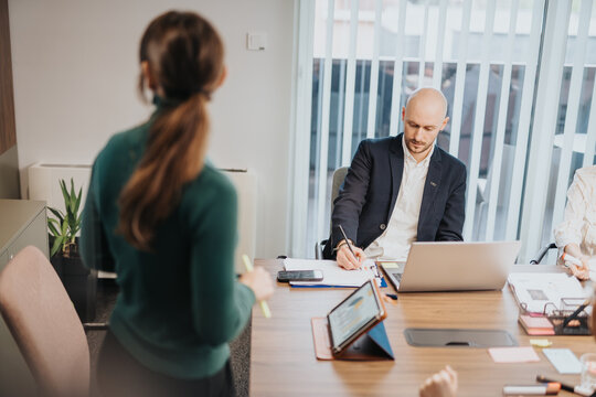 Colleagues collaborate around a table in an office environment, discussing ideas and taking notes, fostering teamwork and productivity in a professional setting.