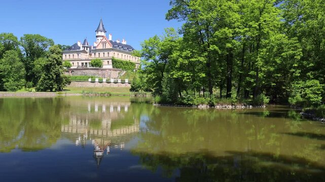 Radun Castle in the Czech Republic, Europe. Castle reflected on still water surrounded by lush greenery against a blue sky on a sunny day.