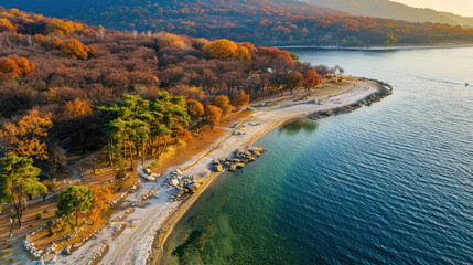 Obraz premium Aerial view of serene lake surrounded by vibrant autumn trees, showcasing peaceful shoreline and clear water