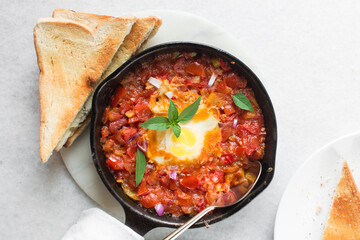 Overhead view of poached egg in tomato sauce, top view of fried egg and tomatoes in a cast iron...
