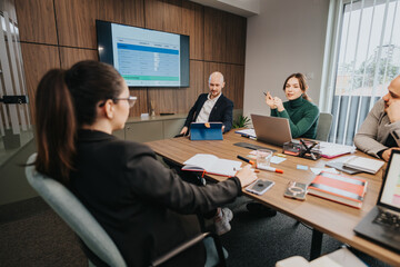 A group of diverse employees working collaboratively in a vibrant, modern office space. They utilize laptops and documents to discuss and strategize in a professional and engaging environment.