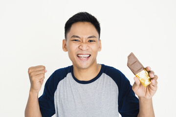 A joyful young man cheerfully holds a chocolate bar, showing excitement and enthusiasm.