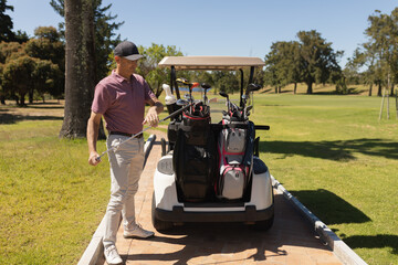 White golf cart sitting on paved cart path through lush green fairway under clear sky