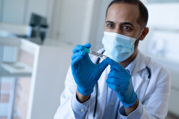 Asian male doctor holding up vaccine vial wearing mask, stethoscope and nitrile gloves in clinic