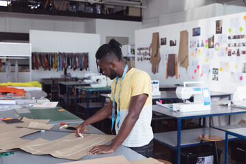 Tailors chalk tracing pattern outlines on green cutting mat in garment studio with sewing machines