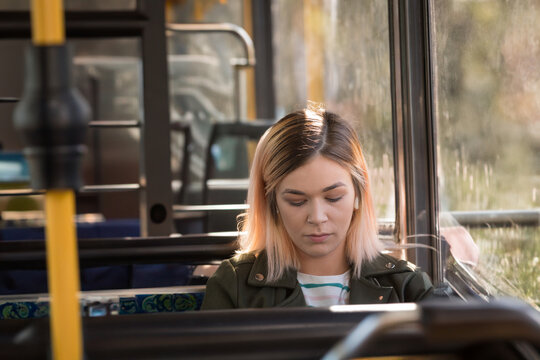 Woman sitting on bus bench seat looking down by patterned bench, yellow pole, sunlit window